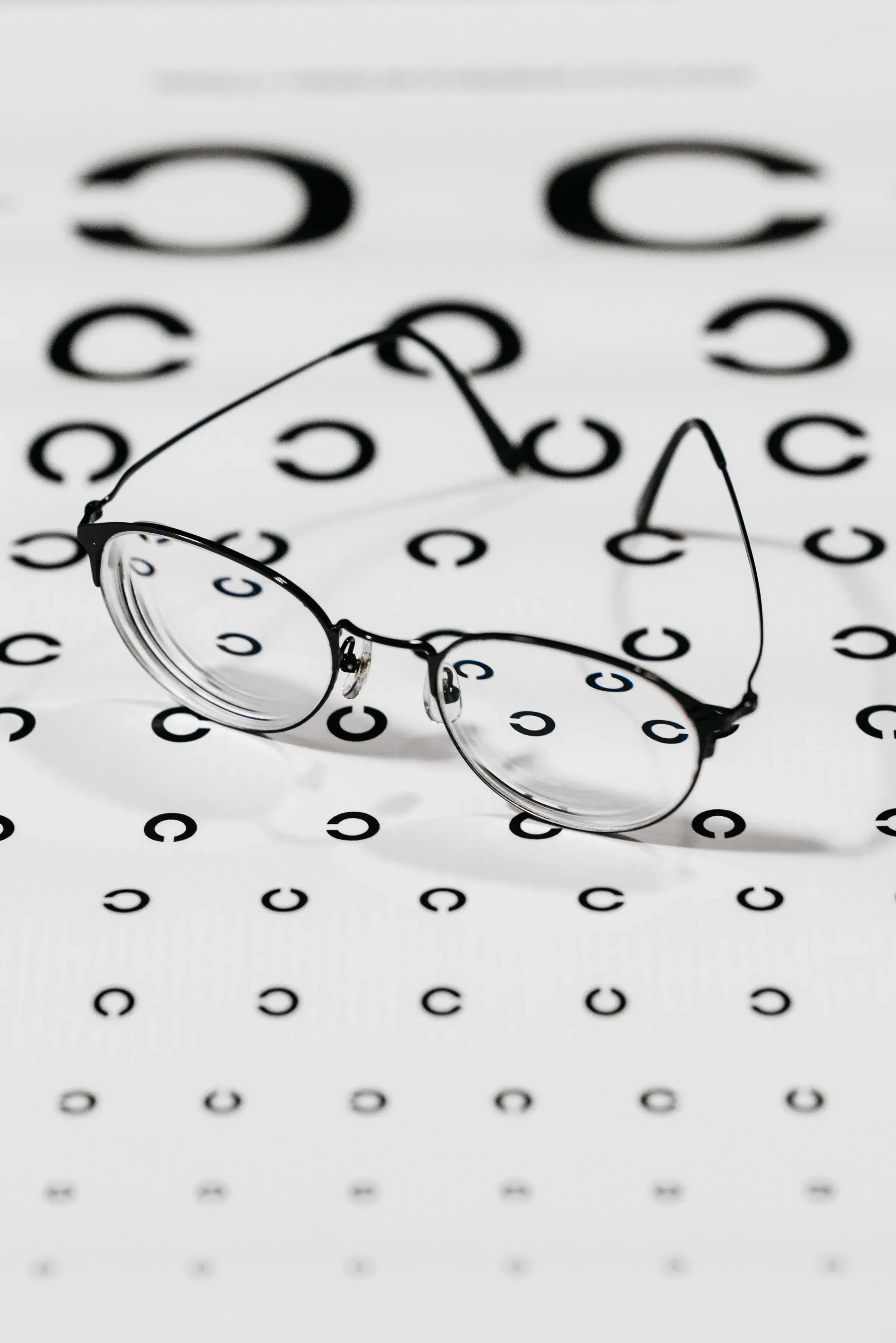 A pair of glasses lying on a visual acuity chart, the rings behind the lenses distorted.