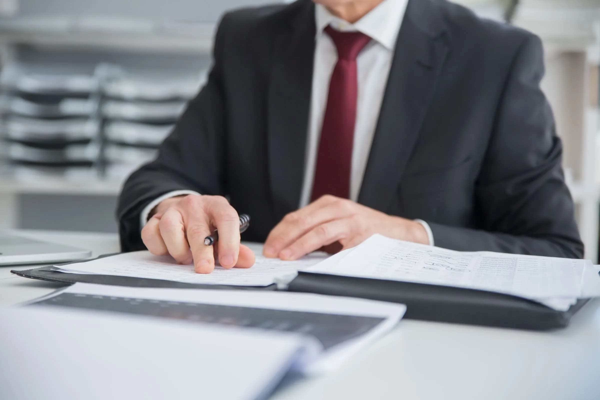 A man in a suit at a desk, pen in hand, working through a printed document.