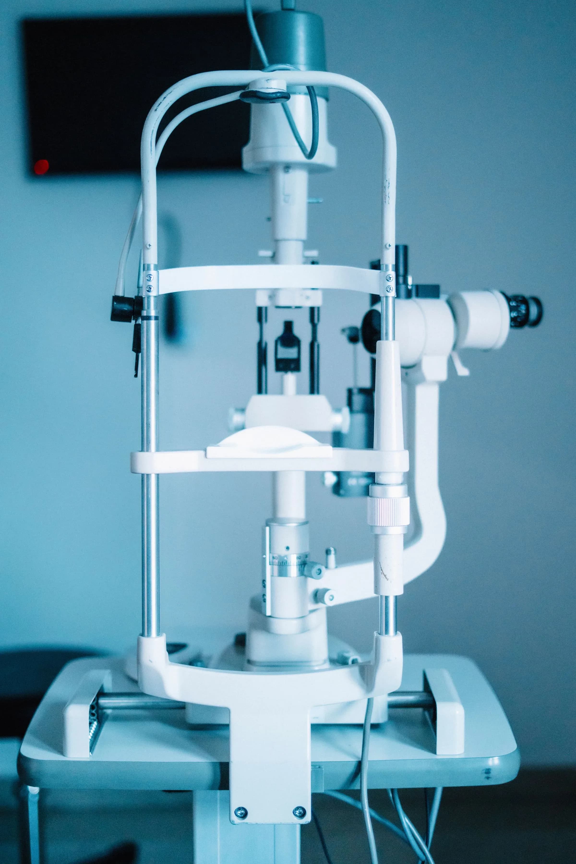 A slit lamp on its stand in an examination room, chin rest and eyepieces close in the frame.