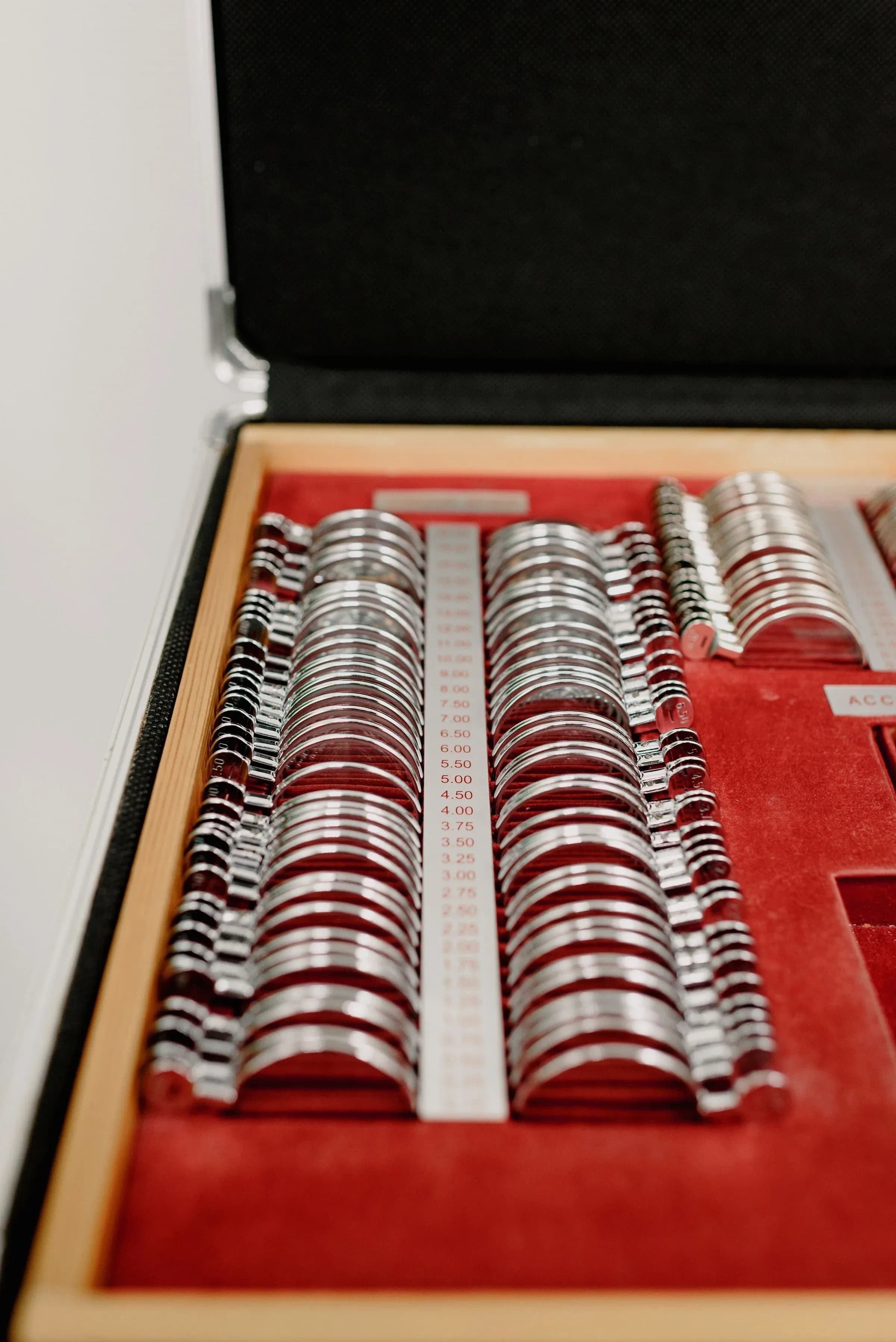 A fitted case of optical trial lenses in graduated rows on red velvet, used to refine a prescription.