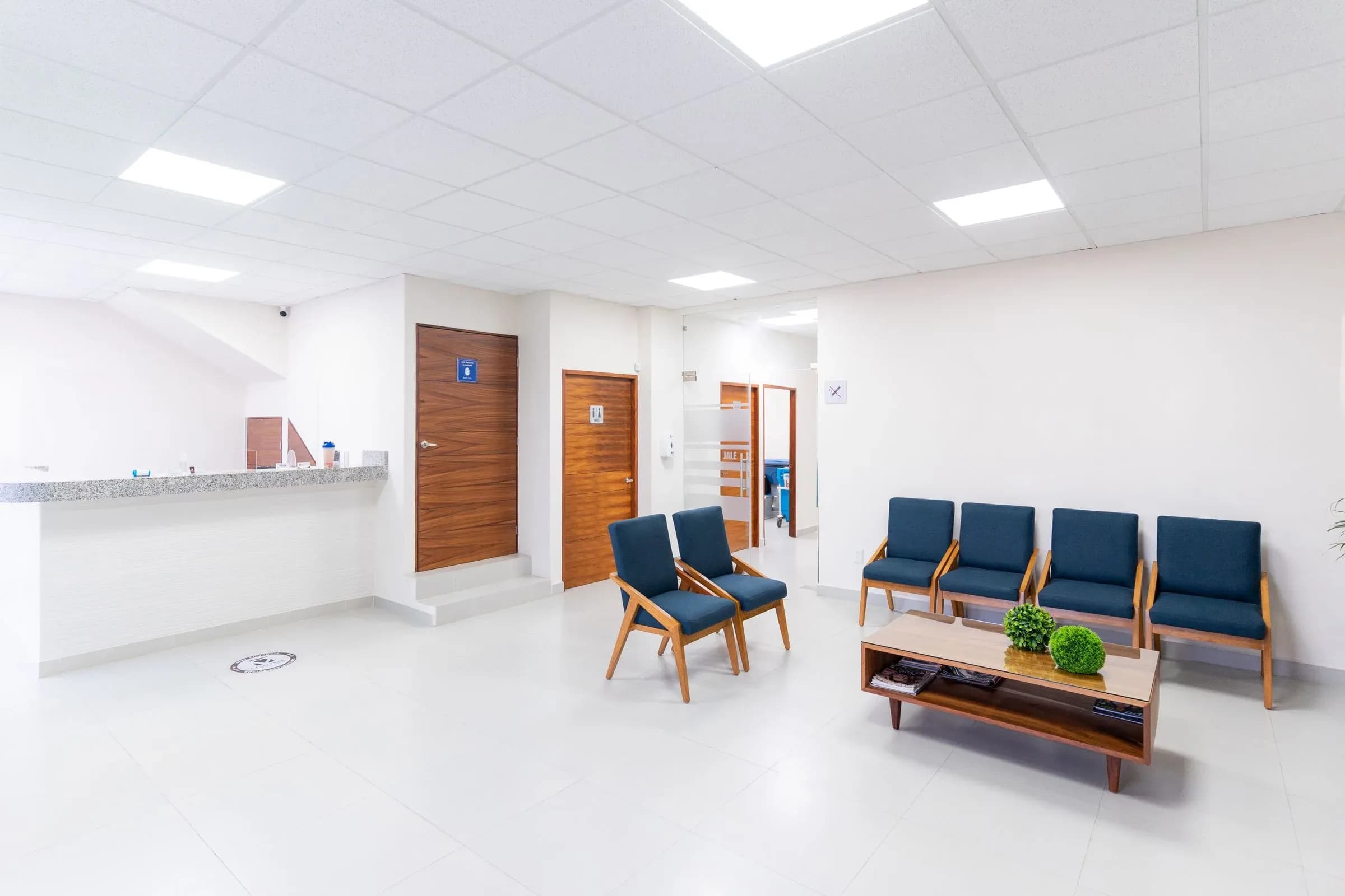 An empty, brightly lit hospital waiting area with blue chairs and a reception desk.