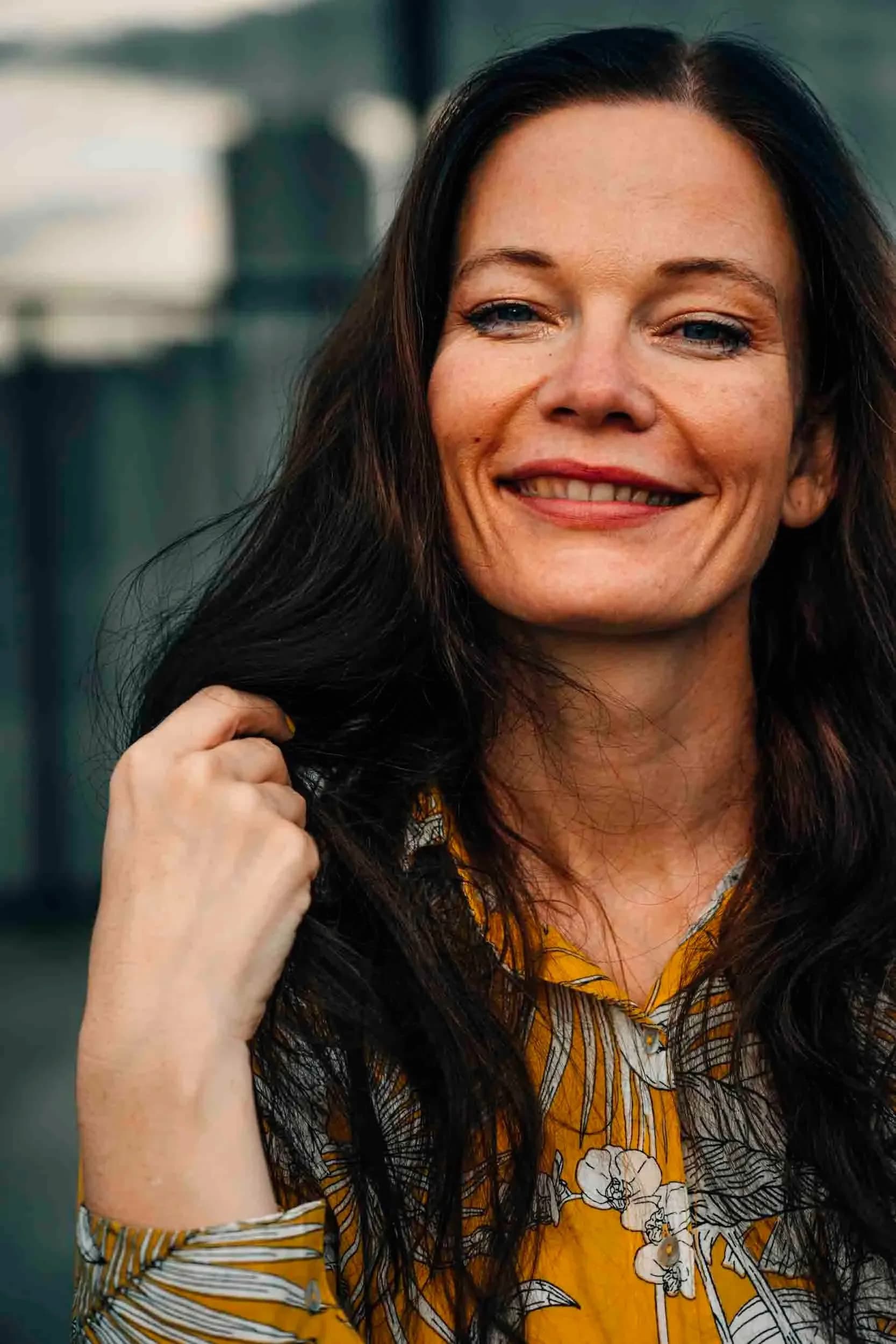 A woman in her forties with long dark hair, laughing, outdoors in soft light.