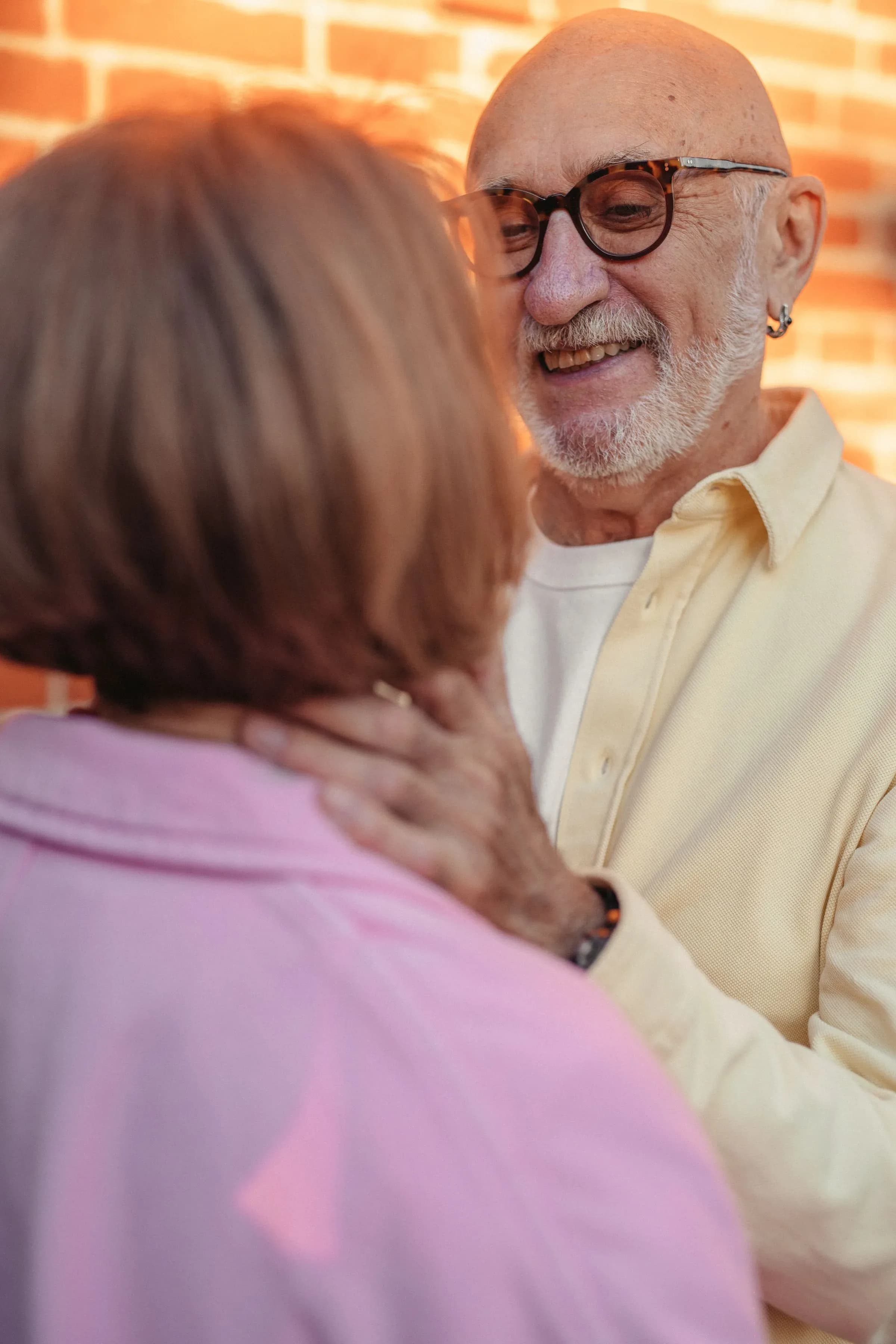 An older man with a white beard and glasses smiling at his partner, close up in warm light.