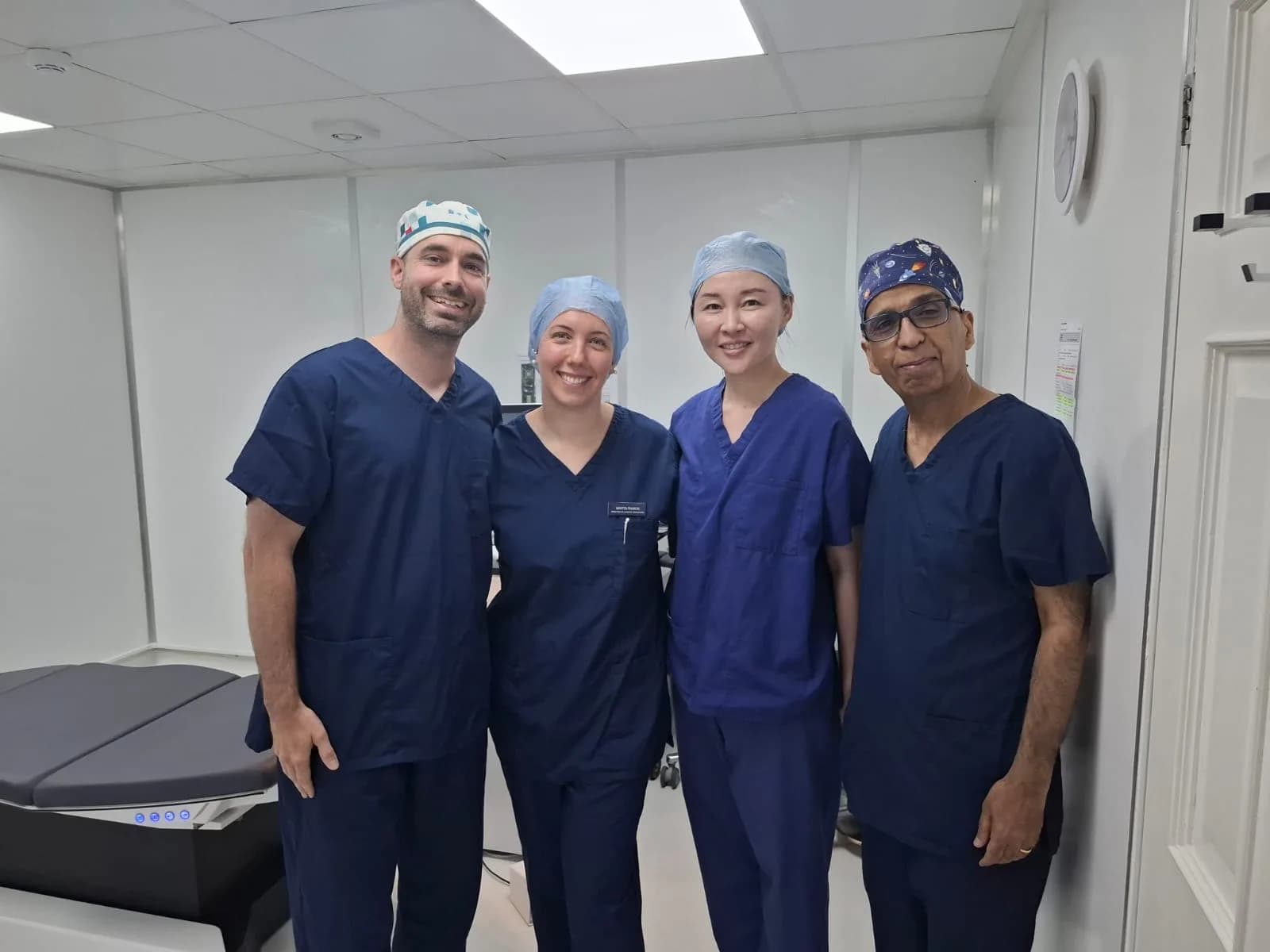 Four members of the theatre team in blue scrubs and surgical caps, including Ms Li Jiang, stand together beside an operating couch.
