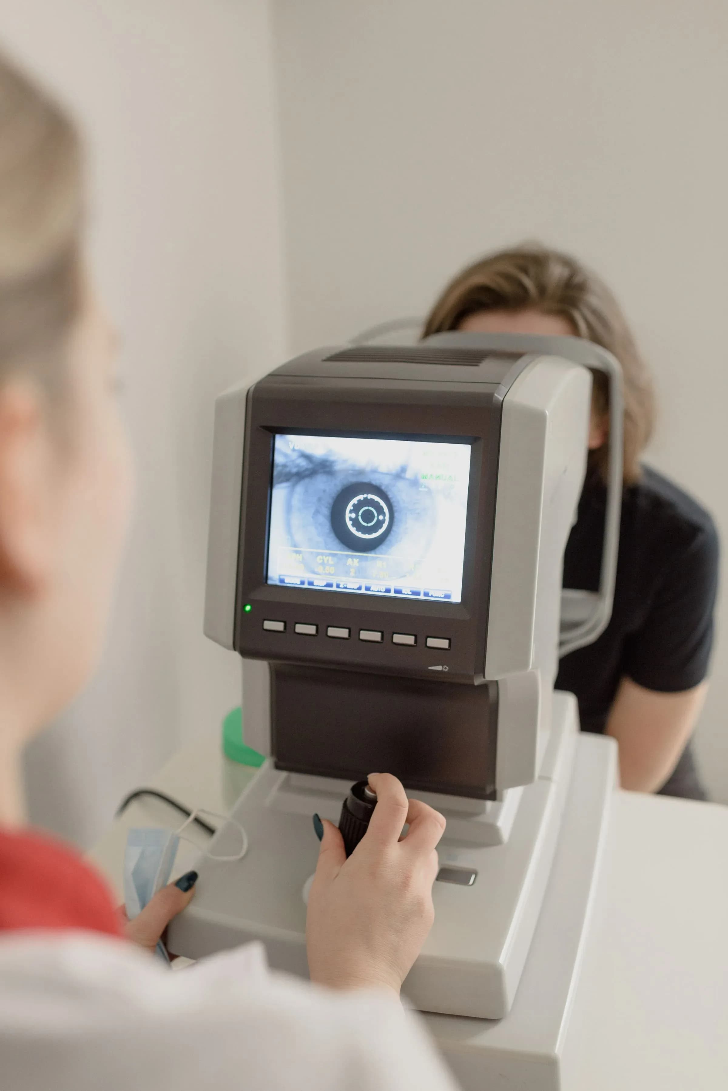 A patient at an autorefractor, an image of their iris shown on the instrument’s screen.
