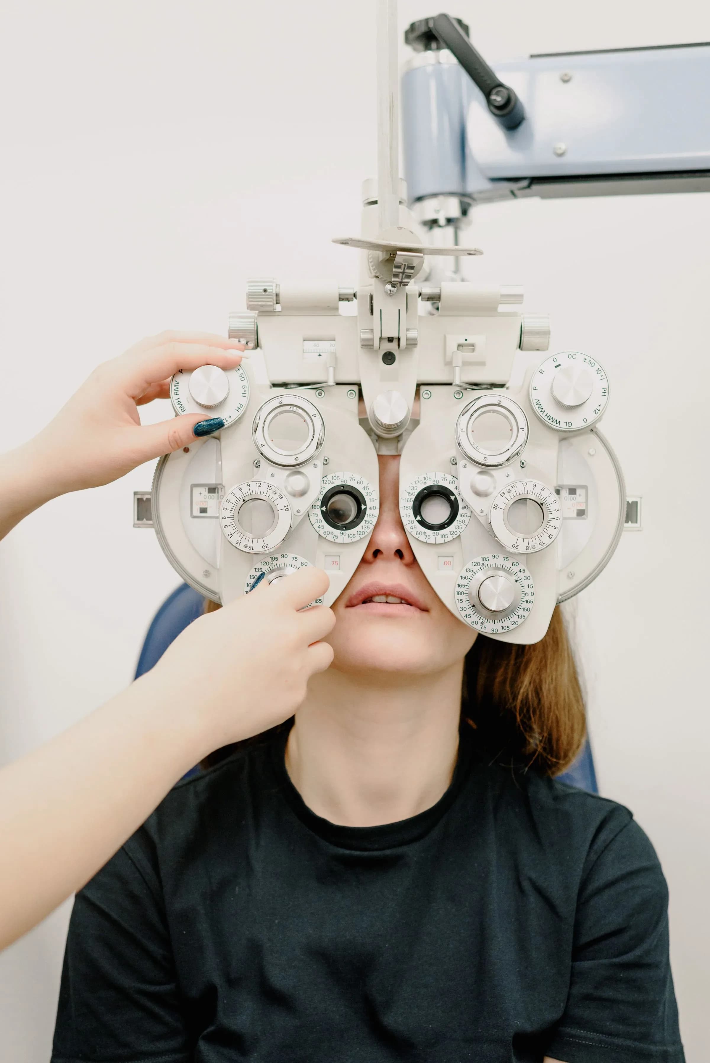 A patient seated behind a phoropter during a sight test, its lens dials filling the frame.