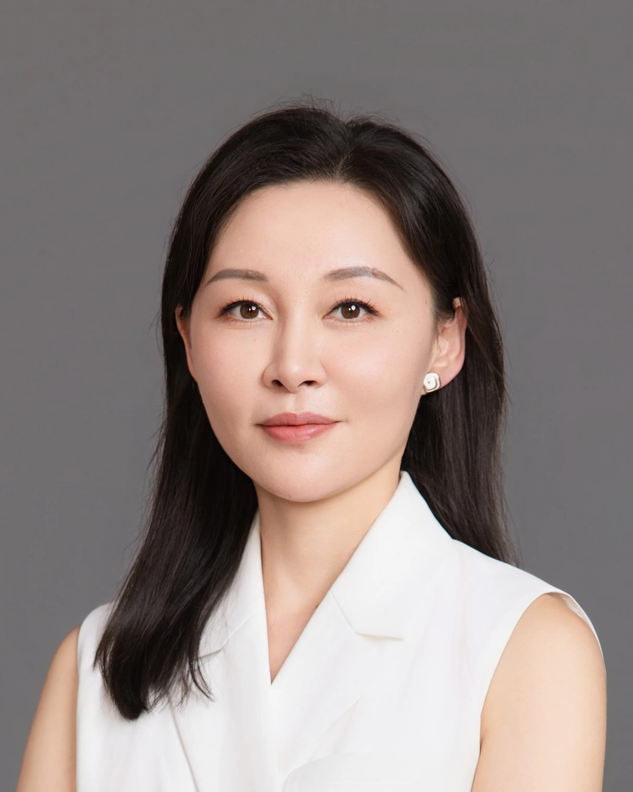 Ms Li Jiang in a white sleeveless jacket with her arms folded, looking levelly at the camera against a plain grey background.