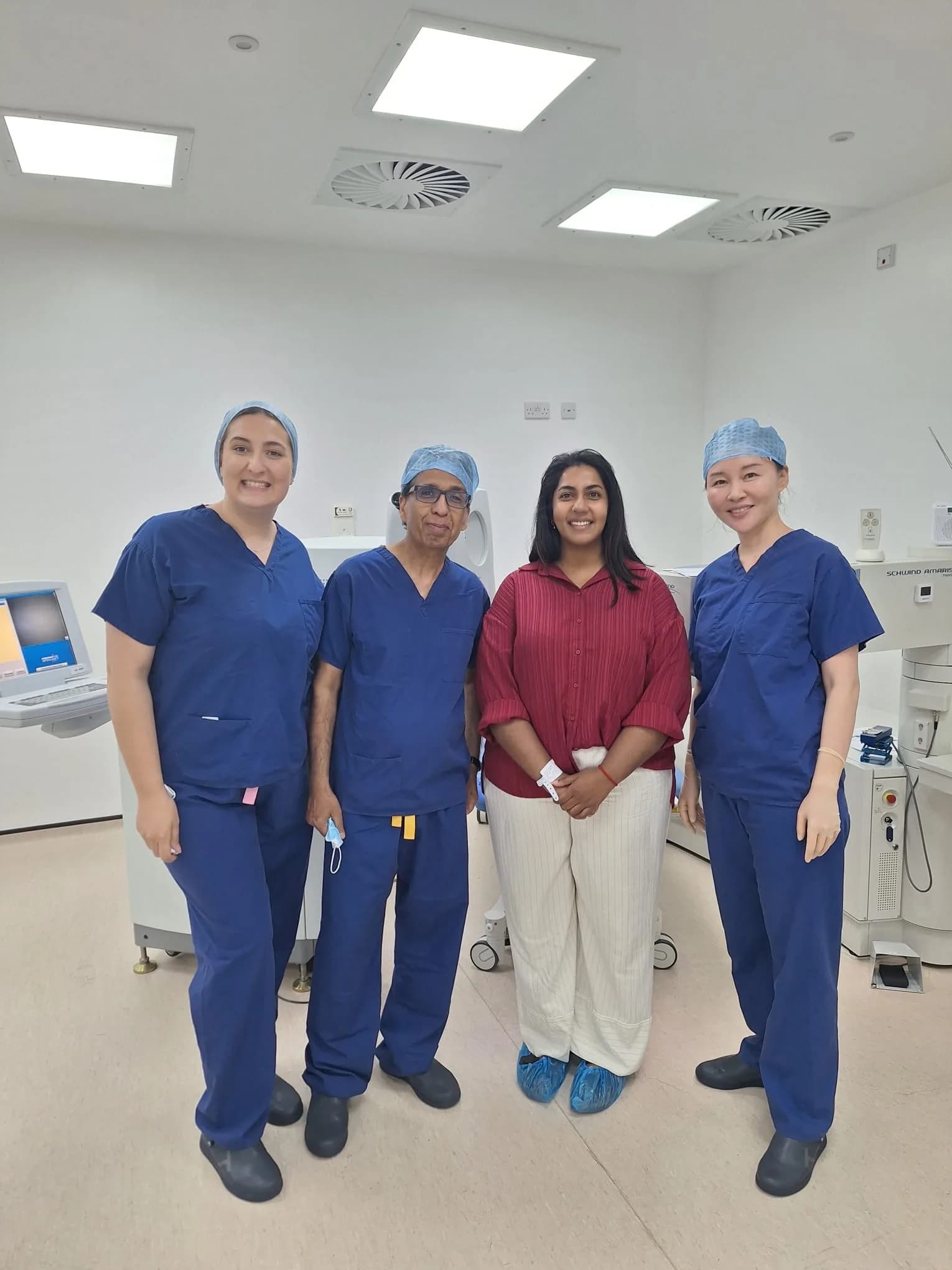 Four members of the theatre team in blue scrubs and surgical caps, including Ms Li Jiang, stand with a patient in day clothes between them.