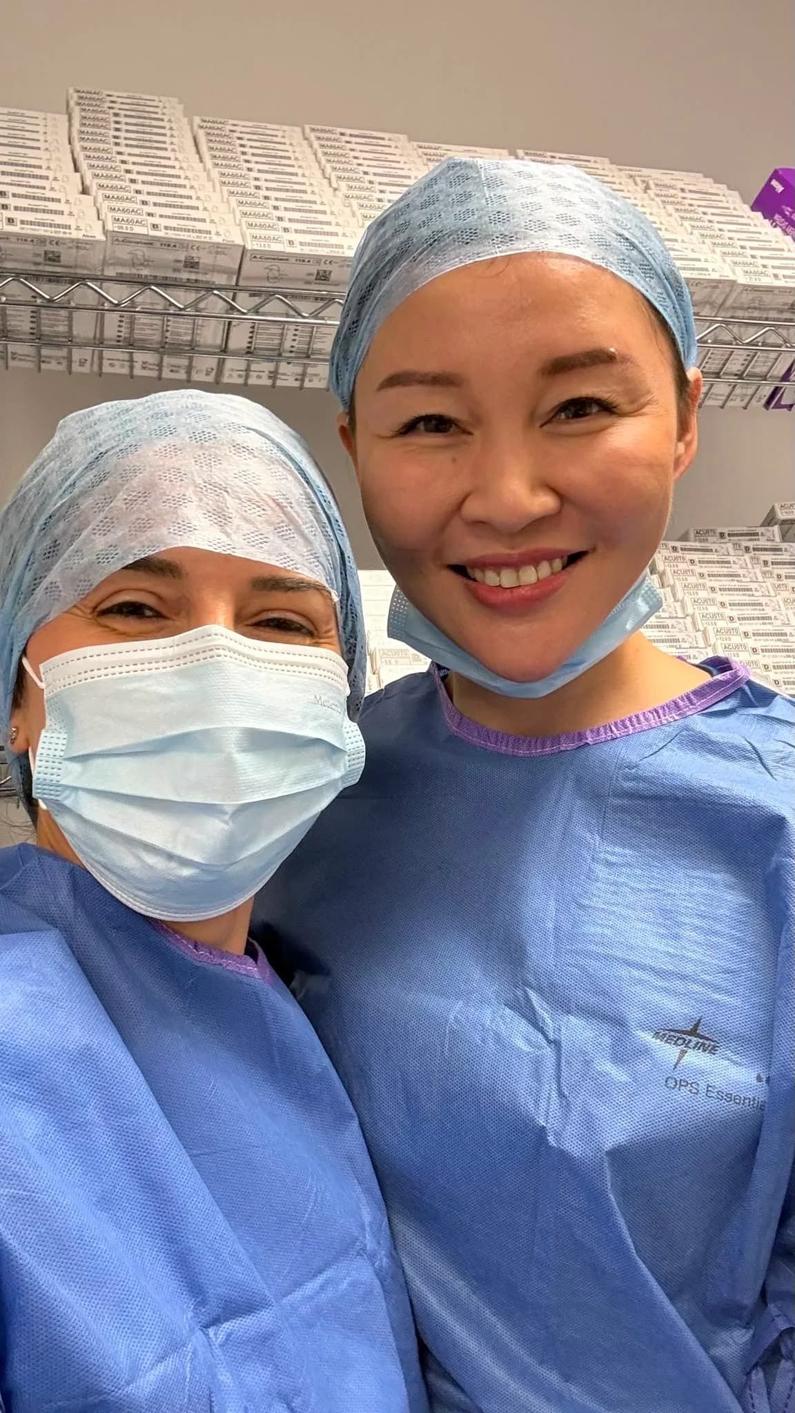 Ms Li Jiang and a colleague in sterile gowns and surgical caps, photographed together before a case; the colleague wears a surgical mask.